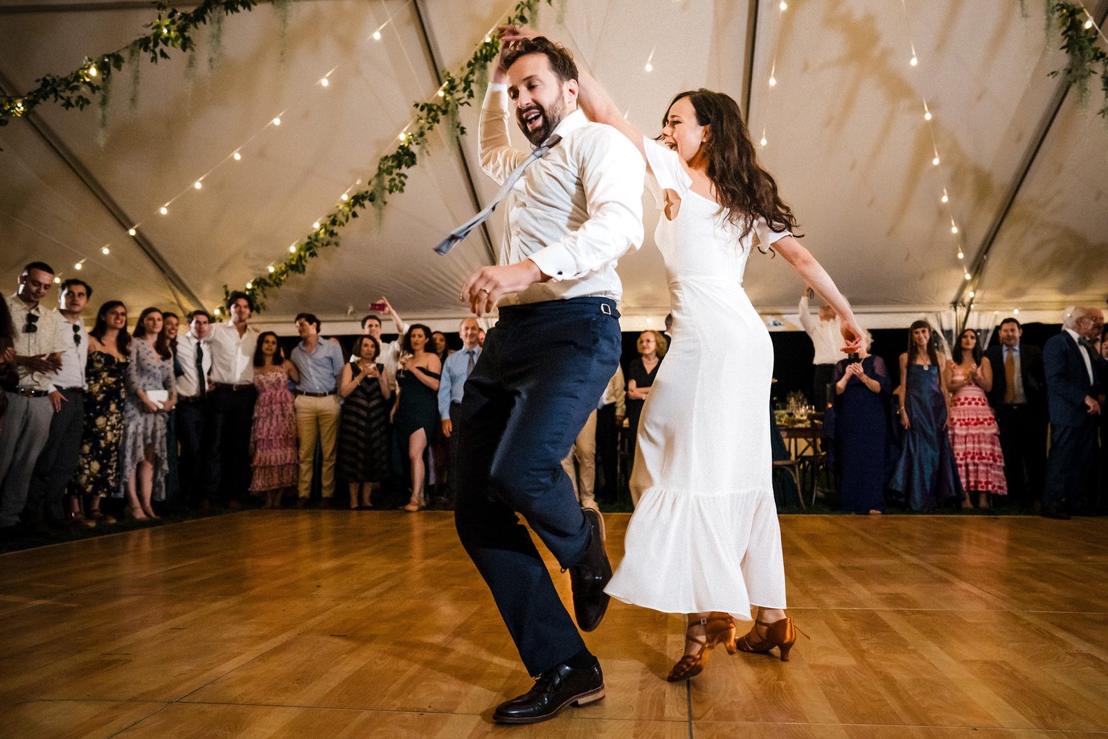 Couple dancing energetically on a wood dance floor at an outdoor tented Portland reception